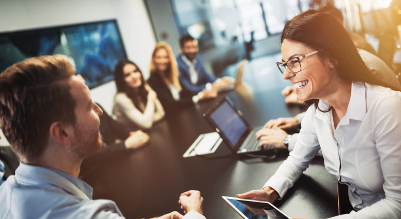 Man and woman talking while team is sitting around conference table