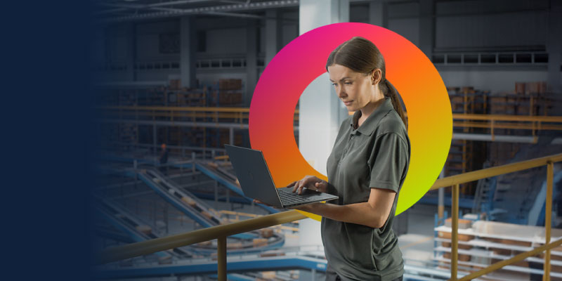 An employee operates a laptop standing in a busy warehouse