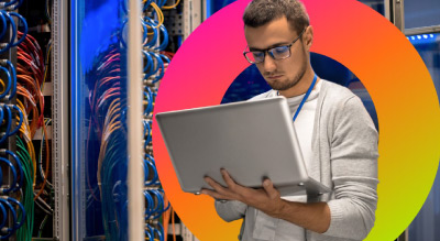 A person holding a laptop in front of a server rack