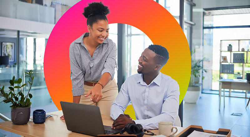 A standing woman points at her sitting coworker's laptop