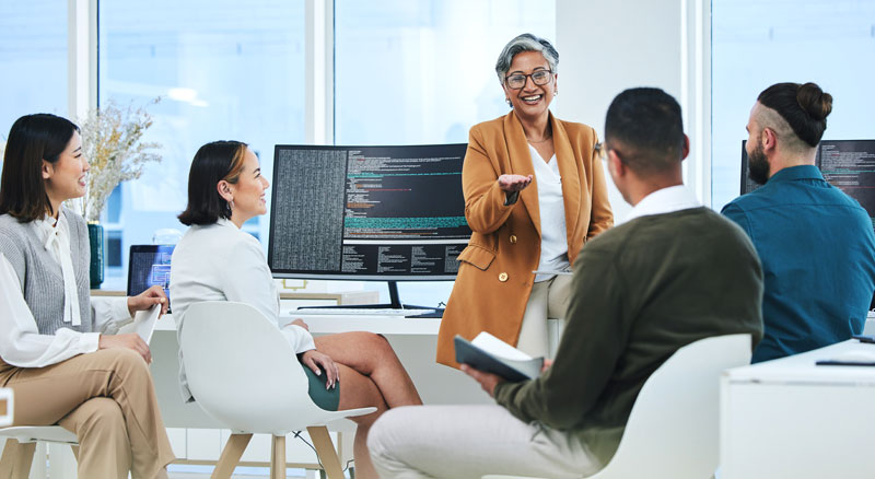 A woman speaks to her team infront of computer monitors