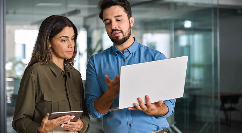 Two office employees share information between a tablet and a laptop