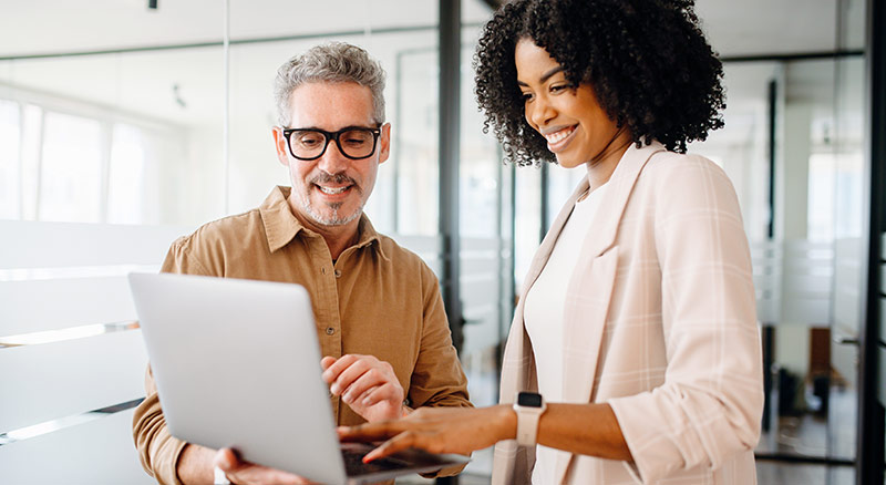 One employee points at information on a laptop that another is holding
