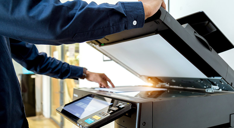 A person is adjusting a document on an open photocopier machine in an office setting