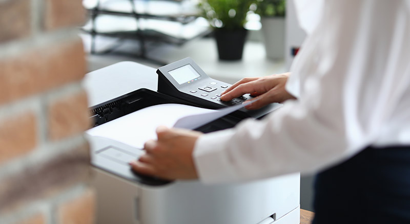 A person in a white blouse is operating a photocopier in an office environment