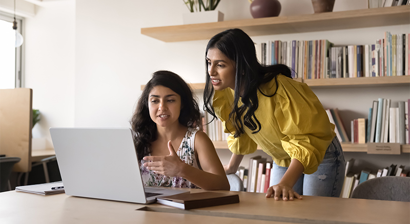 Two individuals discussing something on a laptop at a desk