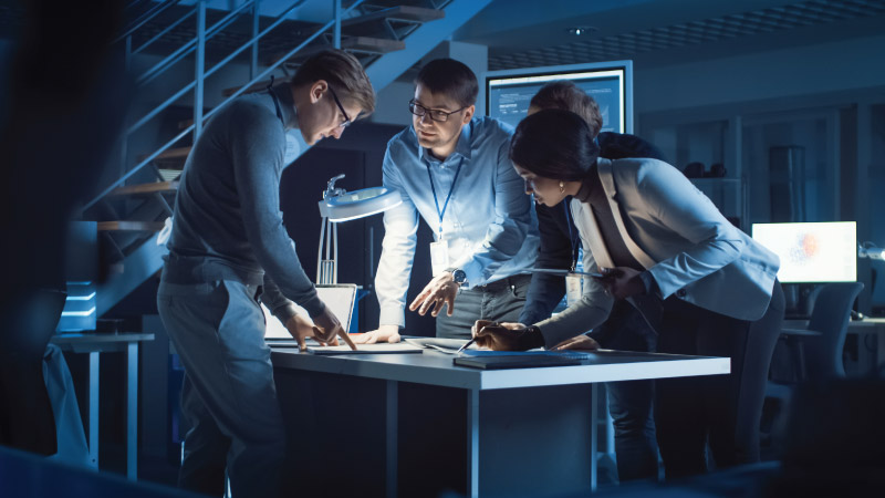Three professionals collaborating over documents on a desk in a dimly lit office environment