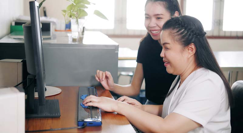 two women in front of computer using assistive keyboard for the blind